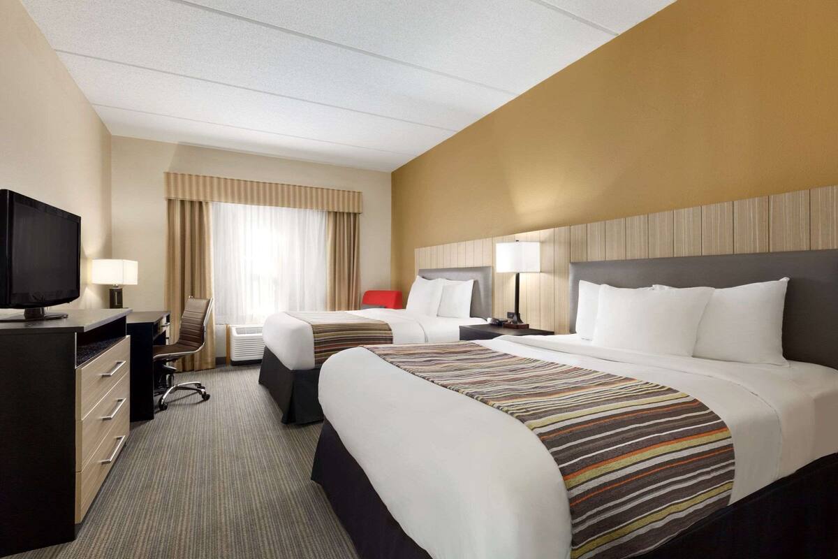 Habitación de hotel con dos camas, un escritorio con televisor, una silla y un ventanal con cortinas.
