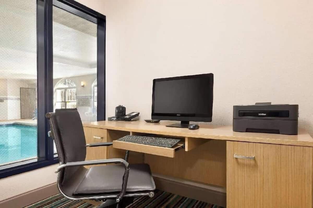 Habitación de hotel con escritorio, computadora, impresora y vista a una piscina.