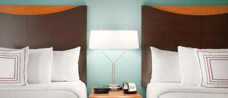 A hotel room with two beds, a nightstand with a lamp, a phone, and a digital clock.
