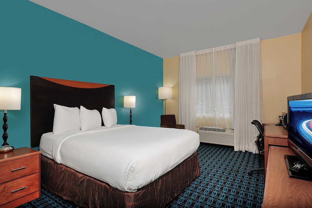 A hotel room with a large bed, two bedside tables with lamps, a television, and a window with curtains.