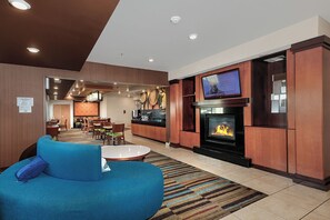 A modern hotel lobby with a fireplace, a television, and a seating area with a blue sofa. - Sonesta Essential Houston Energy Corridor (Houston)