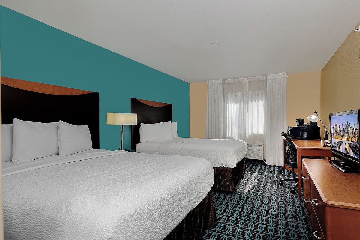 A hotel room with two beds, a desk, a television, and a window with curtains.