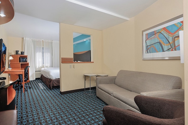 A hotel room with a bed, a sofa, a desk with a lamp, a small table, and a painting on the wall. - Sonesta Essential Houston Energy Corridor (Houston)
