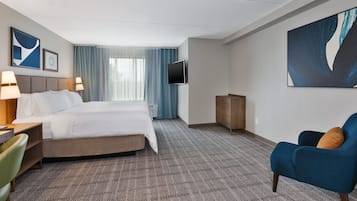Quarto de hotel com cama, escrivaninha, cadeira, televisão e uma grande pintura abstrata na parede.