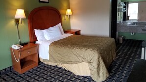 Une chambre d’hôtel comprenant un lit, deux lampes de chevet, une table de chevet avec un téléphone, un tableau encadré au mur et une salle de bain avec un lavabo et un miroir.