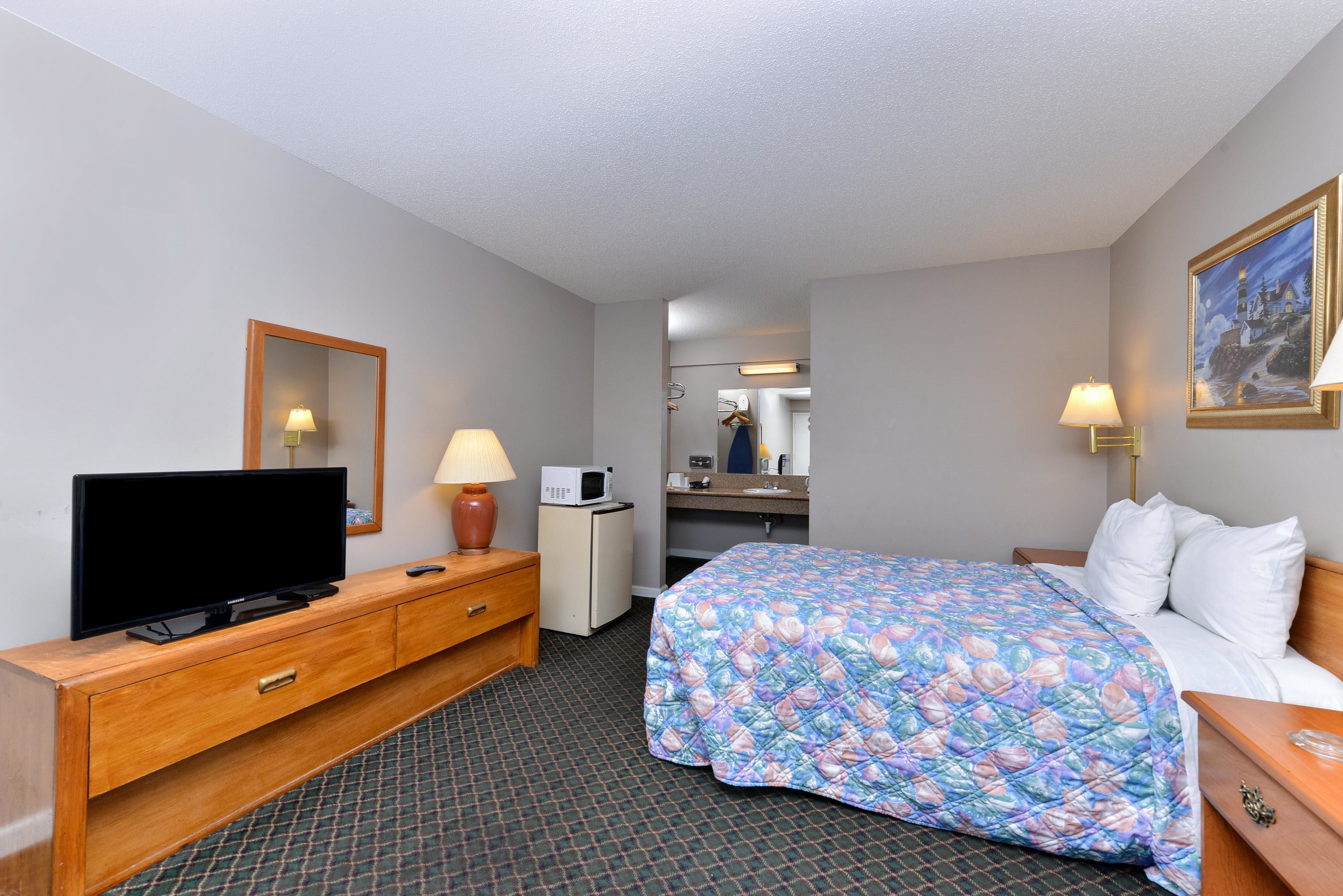 A hotel room with a bed, a TV, a desk with a lamp, a microwave, and a mirror.