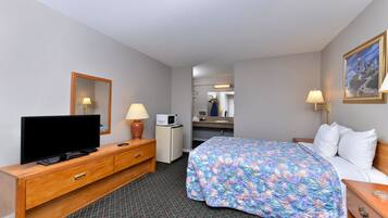 A hotel room with a bed, a TV, a desk with a lamp, a microwave, and a mirror.