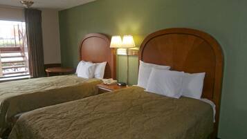 Ein Hotelzimmer mit zwei Betten, jeweils mit einem Holz-Kopfteil und weißen Kissen. An einer Seite befindet sich ein Nachttisch mit einer Lampe und einem Telefon.