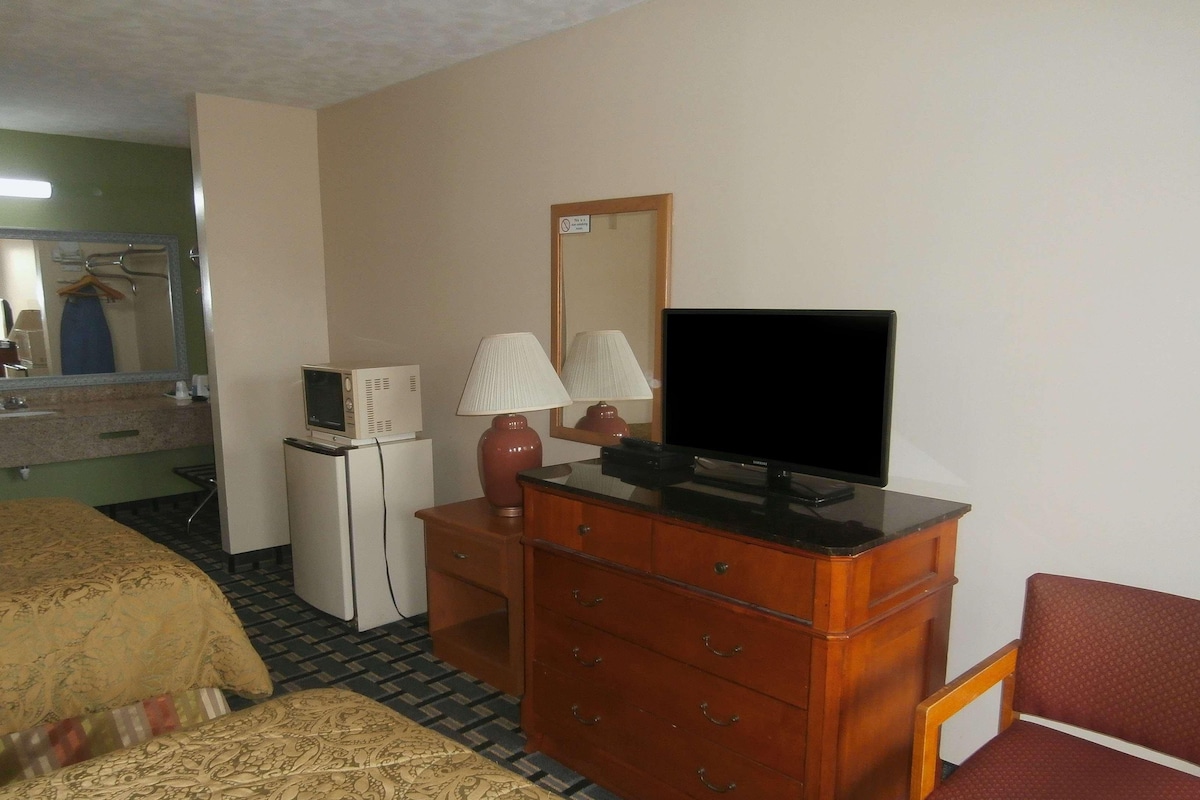 A hotel room with a bed, a dresser with a television, a mirror, and a small refrigerator.