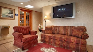 A hotel room with a sofa, armchair, TV, and a breakfast area sign.