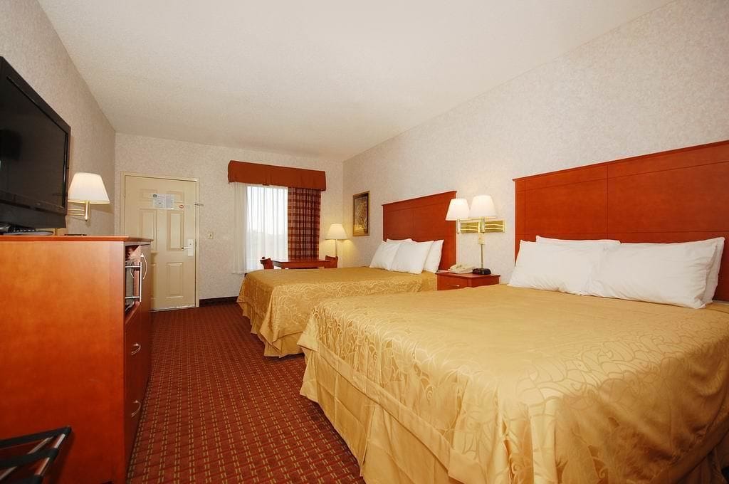 A hotel room with two beds, a TV, a desk, and a window with curtains.