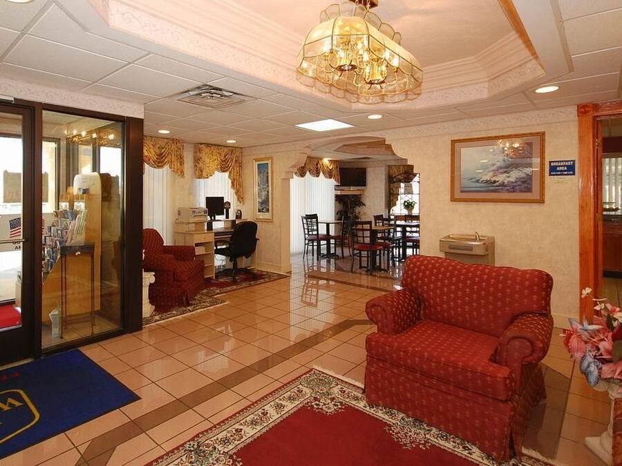 Um saguão de hotel com um sofá vermelho, um candelabro, uma área de refeições e um balcão de recepção.