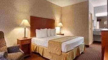 A hotel room with a bed, two bedside tables with lamps, a chair, and a bathroom visible through an open door.