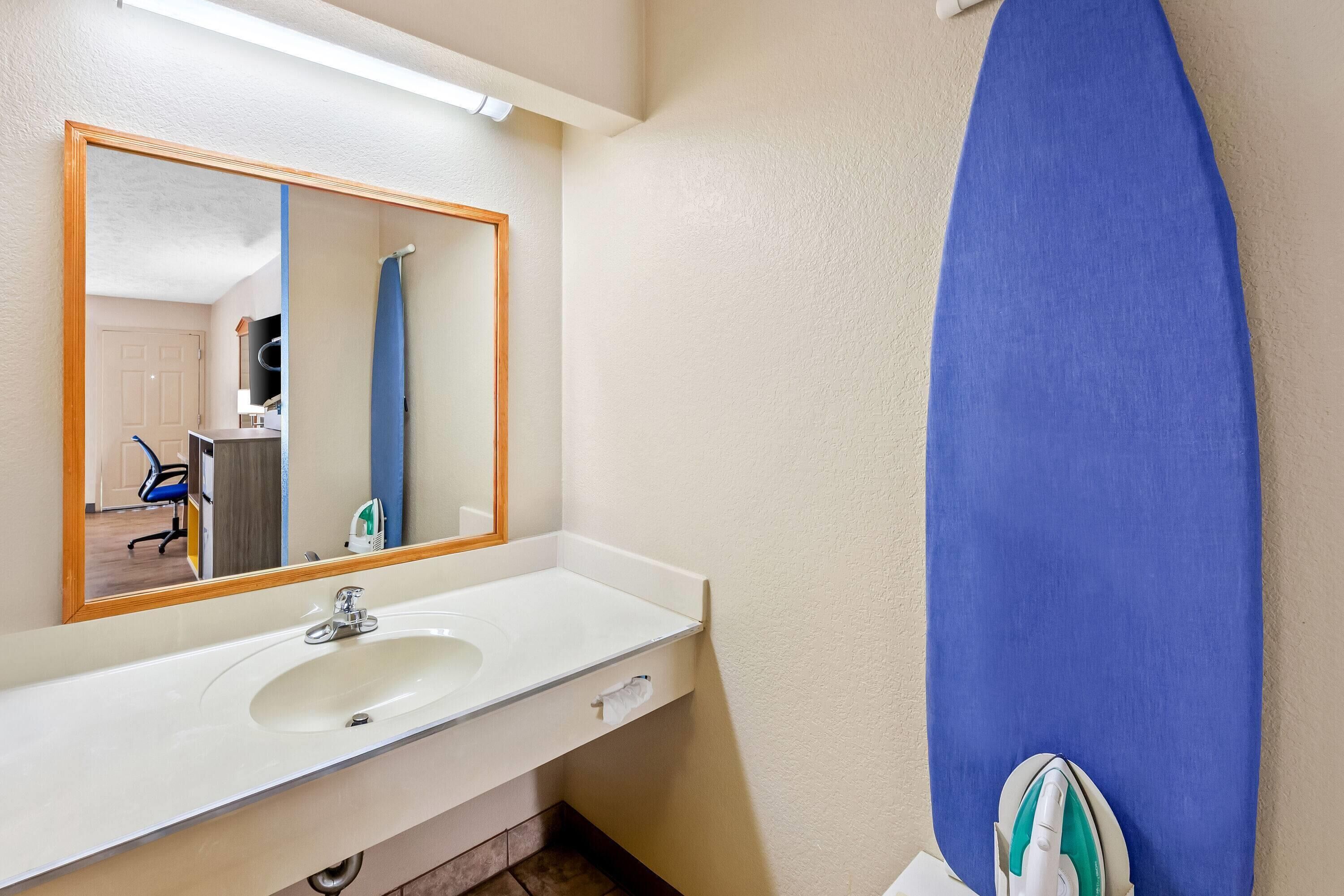 Un baño con un lavamanos blanco, un espejo y una tabla de surf azul apoyada en la pared.