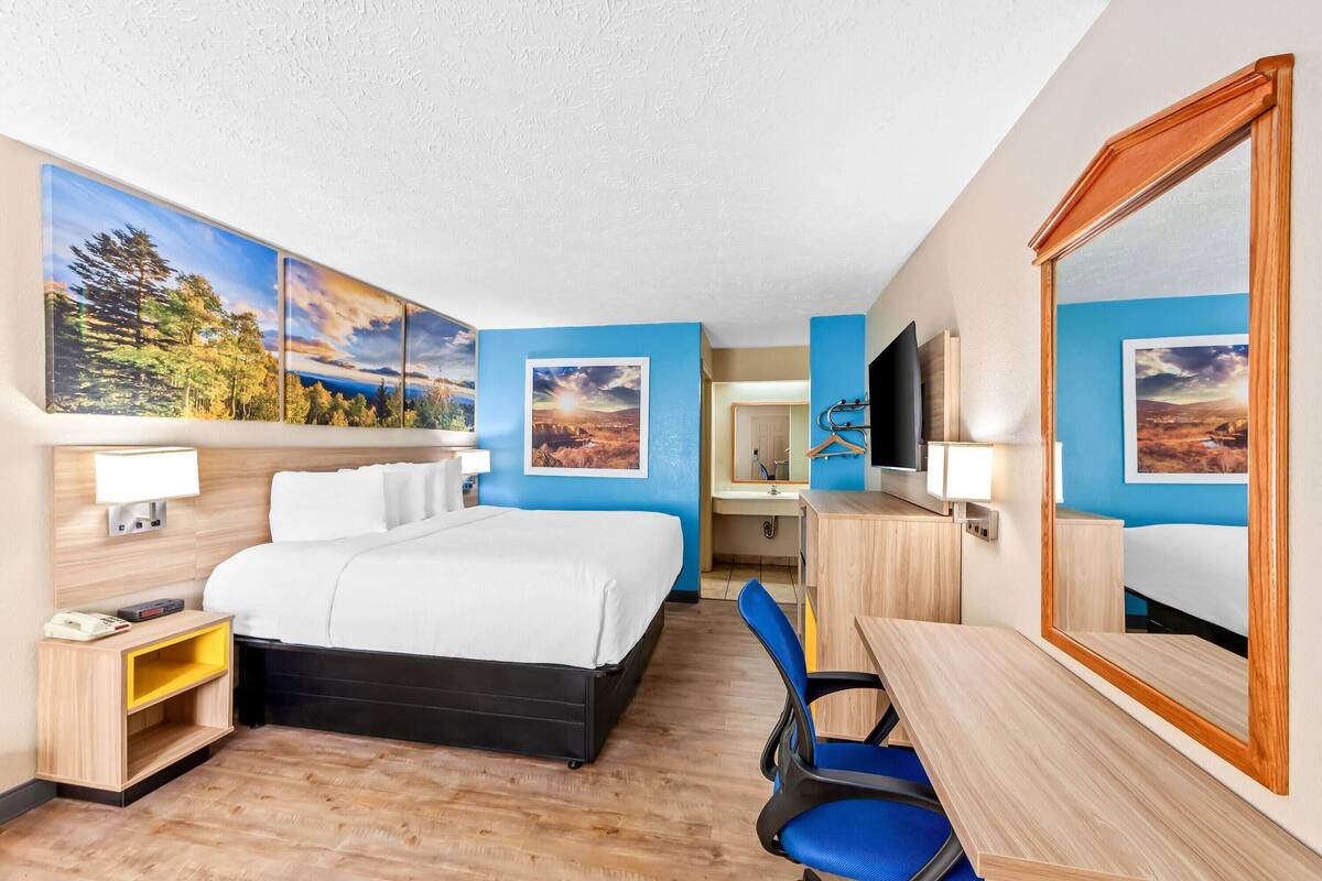 A hotel room with a bed, desk, chair, and artwork on the walls.