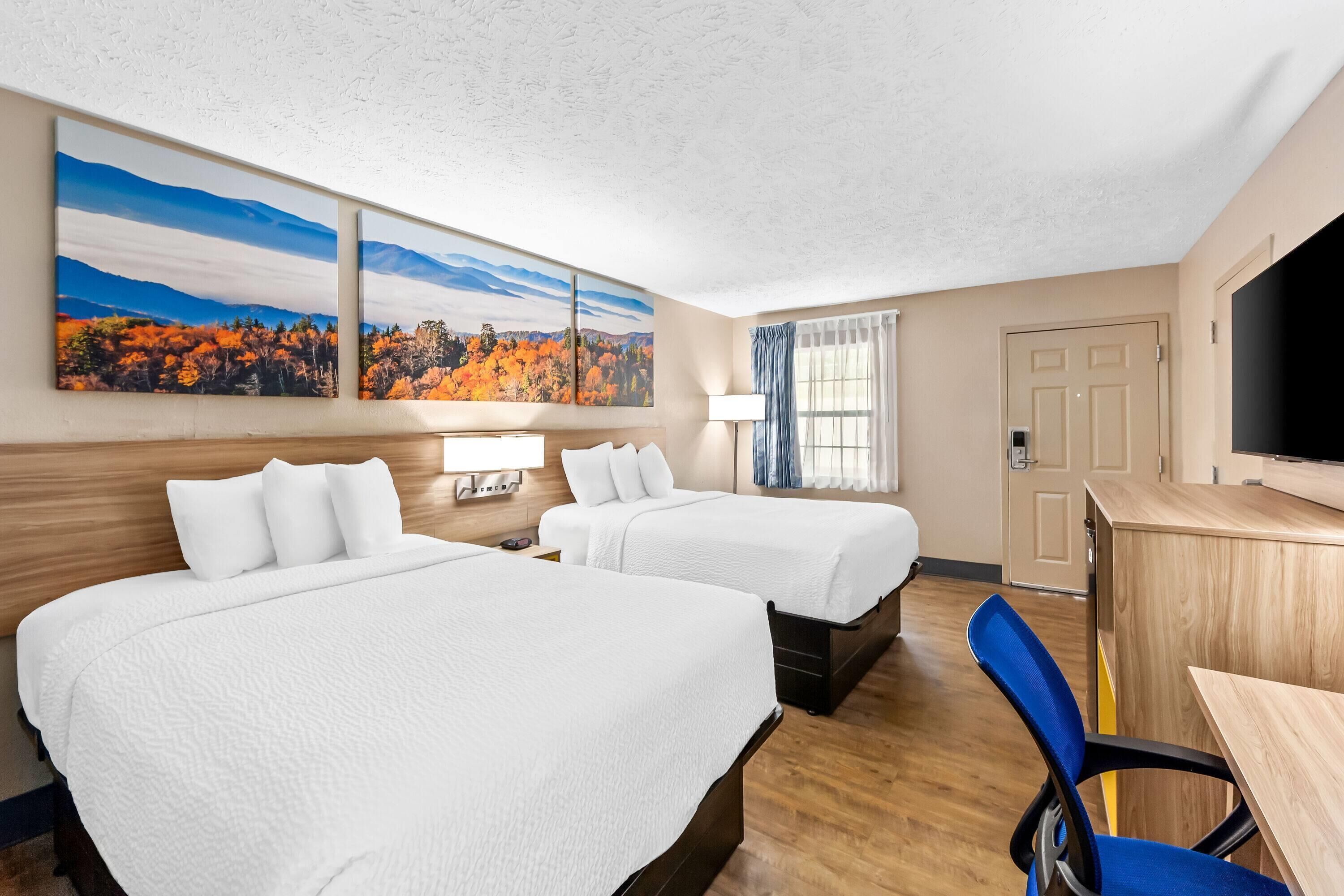 A hotel room with two beds, a desk, a TV, and a window with curtains.