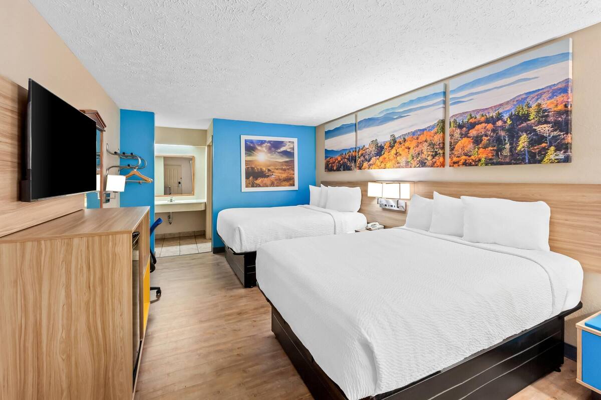 A hotel room with two beds, a desk, a TV, and artwork on the walls.