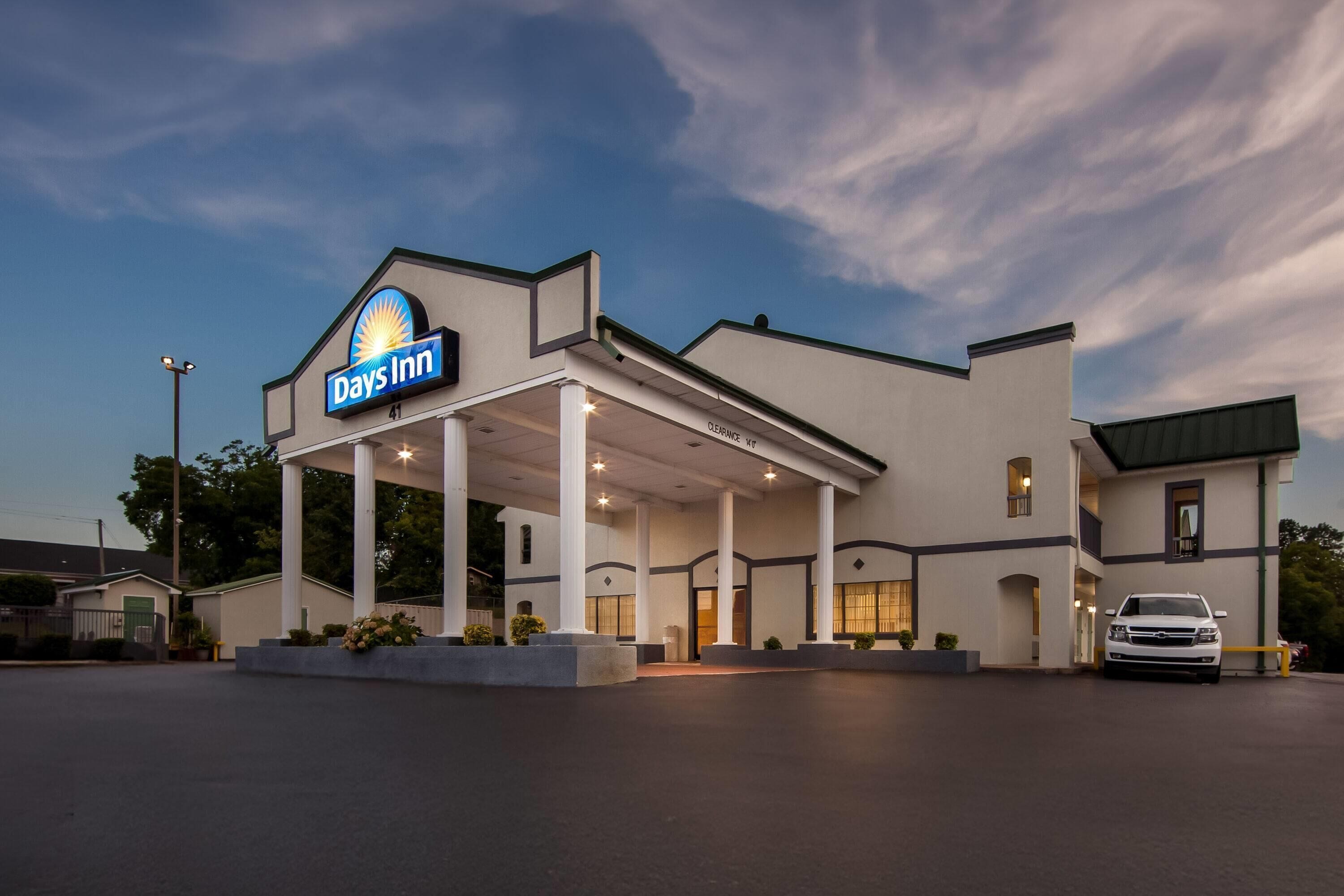 A Days Inn with a covered outdoor area, a car parked in front, and a clear sky.