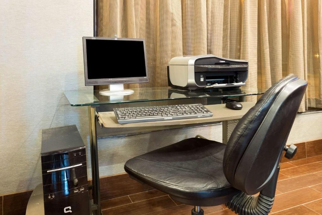 A modern office setup with a glass desk, a computer monitor, a printer, a keyboard, and a leather office chair.