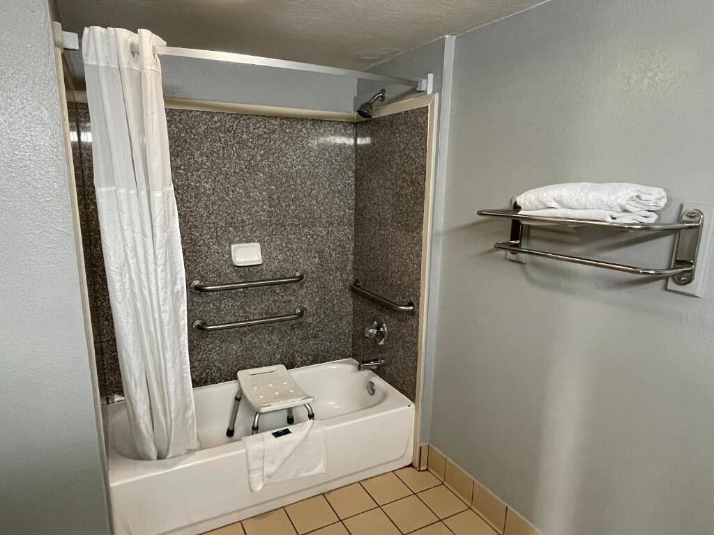 A bathroom with a bathtub, a shower curtain, a towel rack, and a shelf with towels.