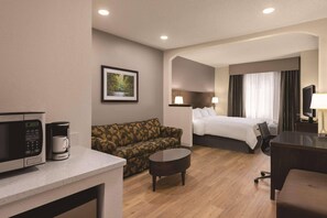 A hotel room with a bed, a sofa, a small table, a desk, a TV, a lamp, a picture on the wall, and a microwave. - Radisson Hotel and Conference Center Rockford (Rockford)