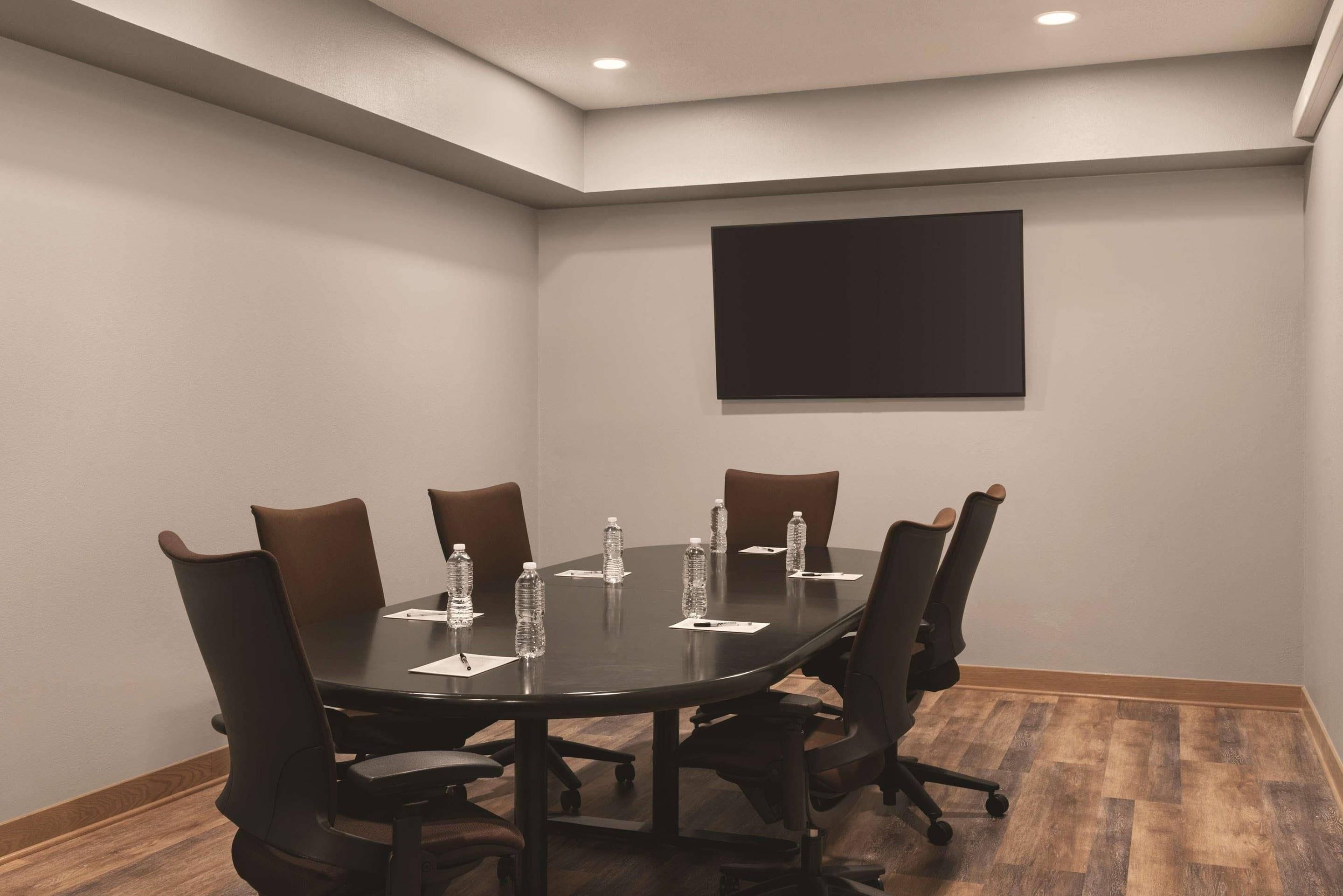 A conference room with a dark table, brown chairs, water bottles, and a black screen on the wall.