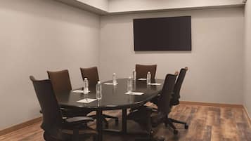 A conference room with a dark table, brown chairs, water bottles, and a black screen on the wall.