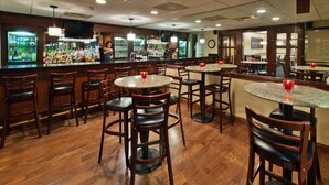 A bar area with multiple round tables and chairs, a bar counter with a variety of bottles, and a television mounted on the wall. - Radisson Hotel and Conference Center Rockford (Rockford)