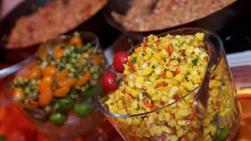 A buffet with a variety of dishes including a fruit salad with diced pineapple and red bell peppers, and a dish with cherry tomatoes.