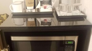 Angolo cottura compatto con forno a microonde e mini-frigorifero, dotato di macchina da caffè e bollitore sul piano di lavoro.