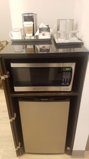 A compact kitchen setup with a microwave and a mini-fridge, featuring a coffee maker and a kettle on the countertop. - Radisson Hotel and Conference Center Rockford (Rockford)