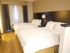 Een hotelkamer met twee bedden, een nachtkastje met een lamp en een raam met gordijnen.