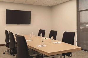 A conference room with a long table, six chairs, water bottles, and a flat-screen TV on the wall. - Radisson Hotel and Conference Center Rockford (Rockford)