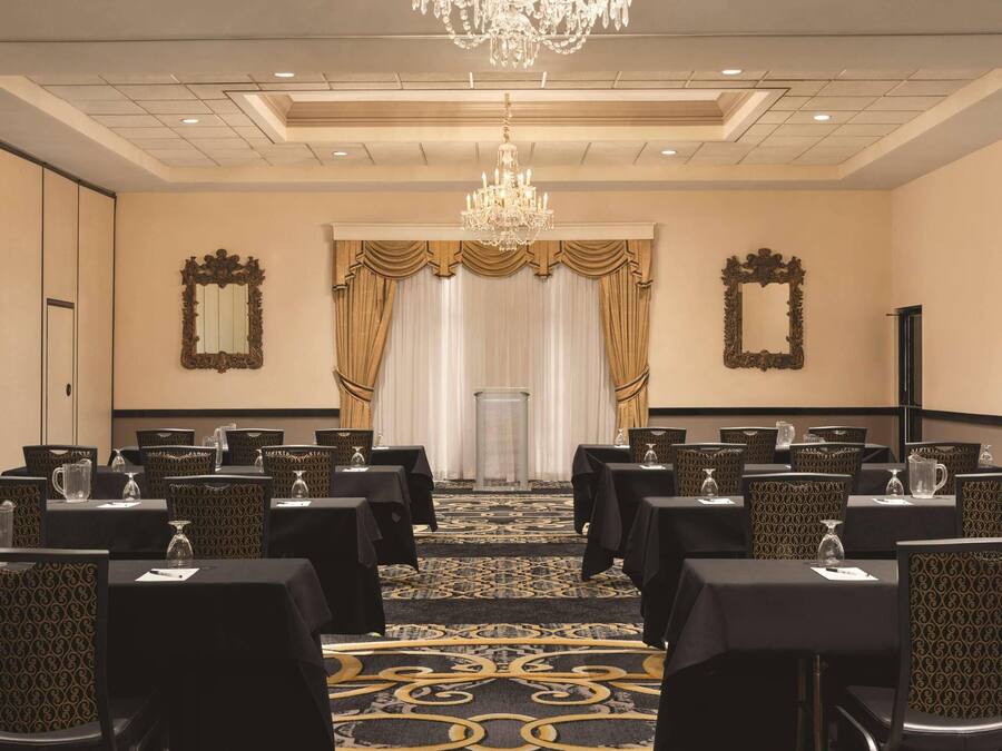 Un salón de conferencias con mesas, sillas, una araña y cortinas.