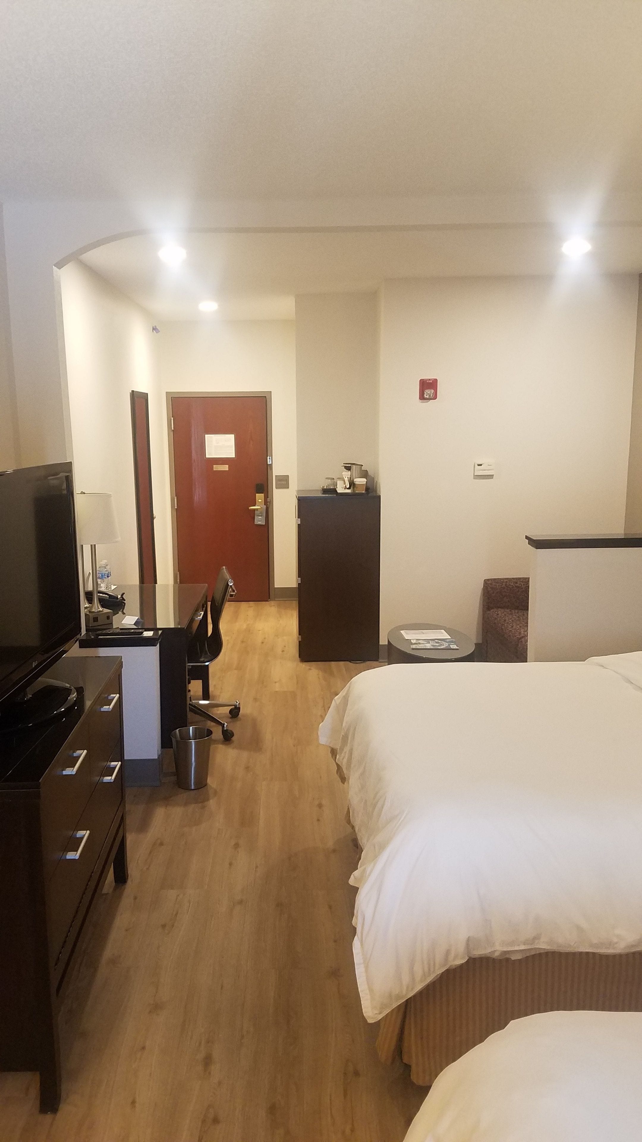 Een hotelkamer met een bed, een bureau met een computer, een televisie en een kleine kitchenette.