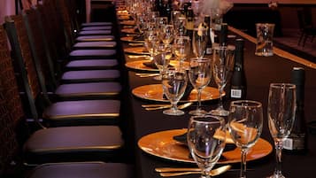 Una larga mesa de banquete dispuesta con múltiples copas de vino, platos y cubiertos, flanqueada por filas de sillas.