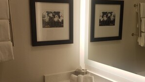 Un bagno con un lavandino bianco, uno specchio, due quadri appesi al muro e un water.