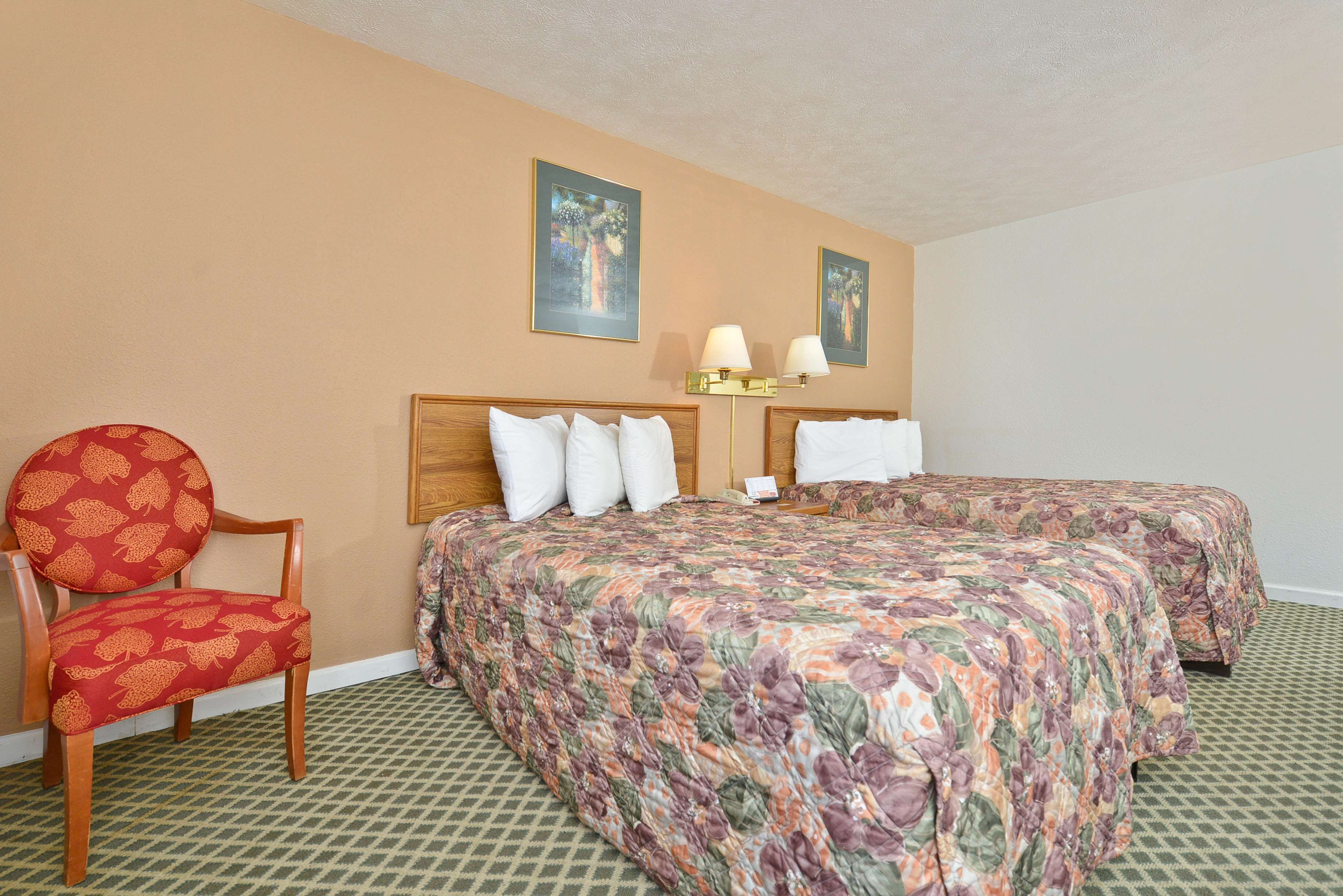 A hotel room with a bed, two bedside tables, a chair, and a wall-mounted lamp.