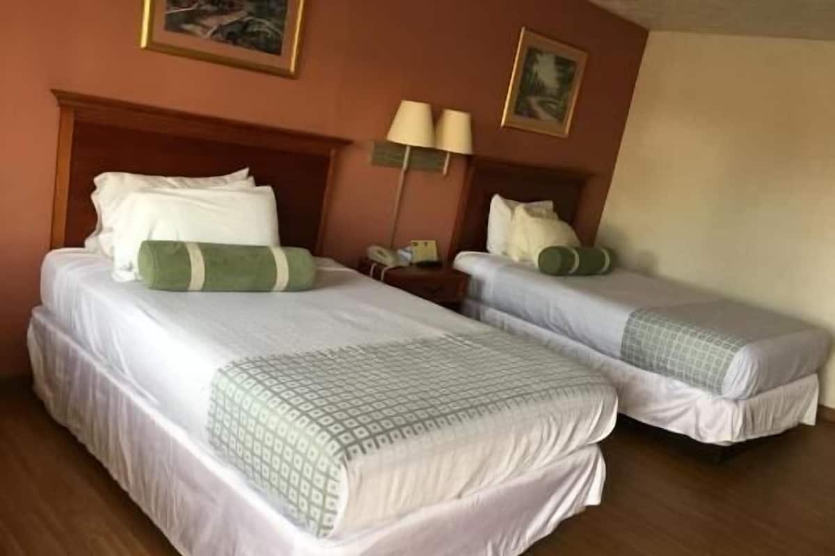 Une chambre d’hôtel avec deux lits, chacun agrémenté de draps blancs et d’oreillers verts, une tête de lit en bois, une table de chevet avec des lampes et un tableau encadré au mur.