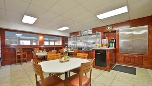 A dining area with a white table and chairs, a kitchen area with stainless steel appliances, and a clock on the wall.