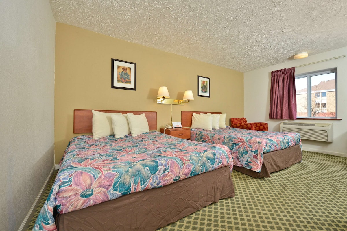 Une chambre d’hôtel avec deux lits, une fenêtre donnant sur un paysage agréable, une lampe fixée au mur et un tableau encadré.