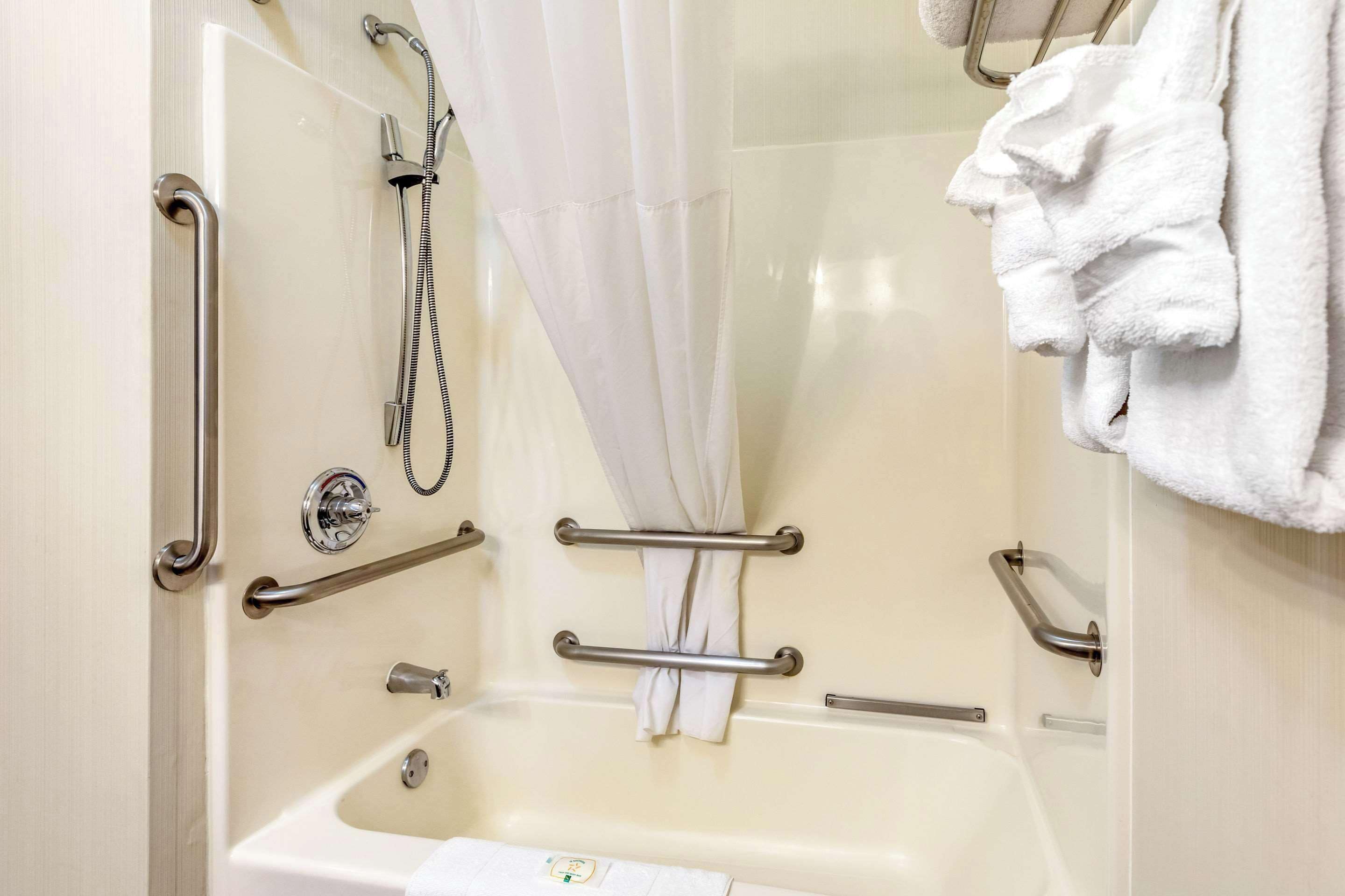 A bathroom with a bathtub, shower, and handrails.