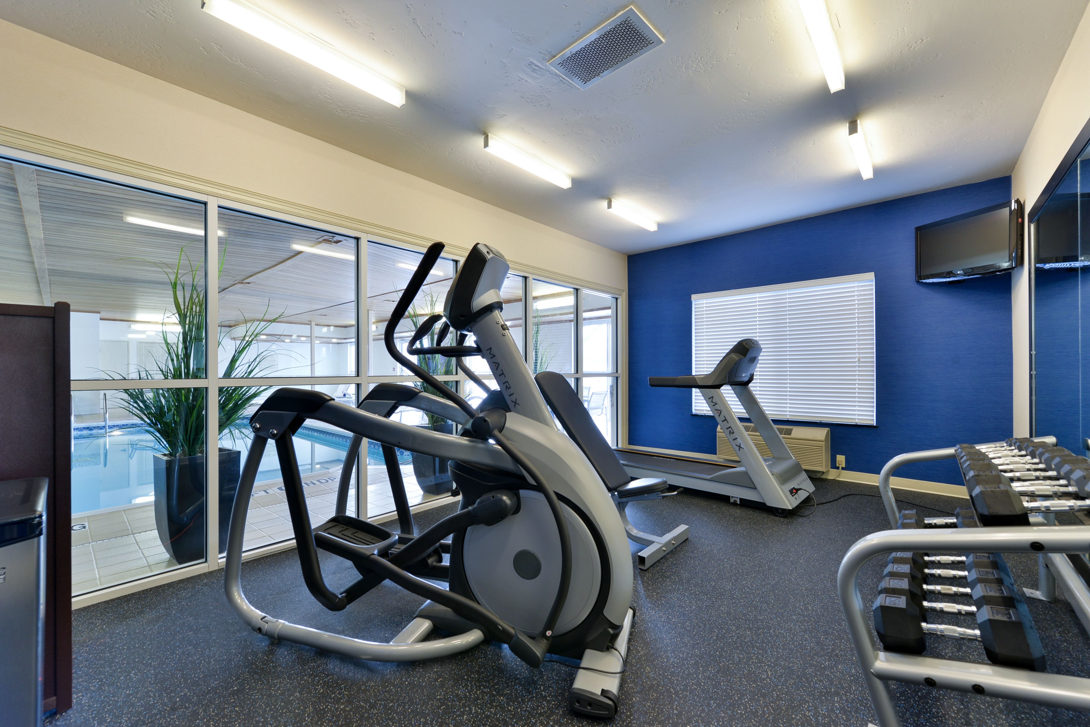 A fitness room with exercise equipment, large windows, and a blue wall.