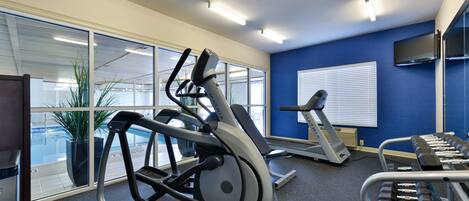 A fitness room with exercise equipment, large windows, and a blue wall.