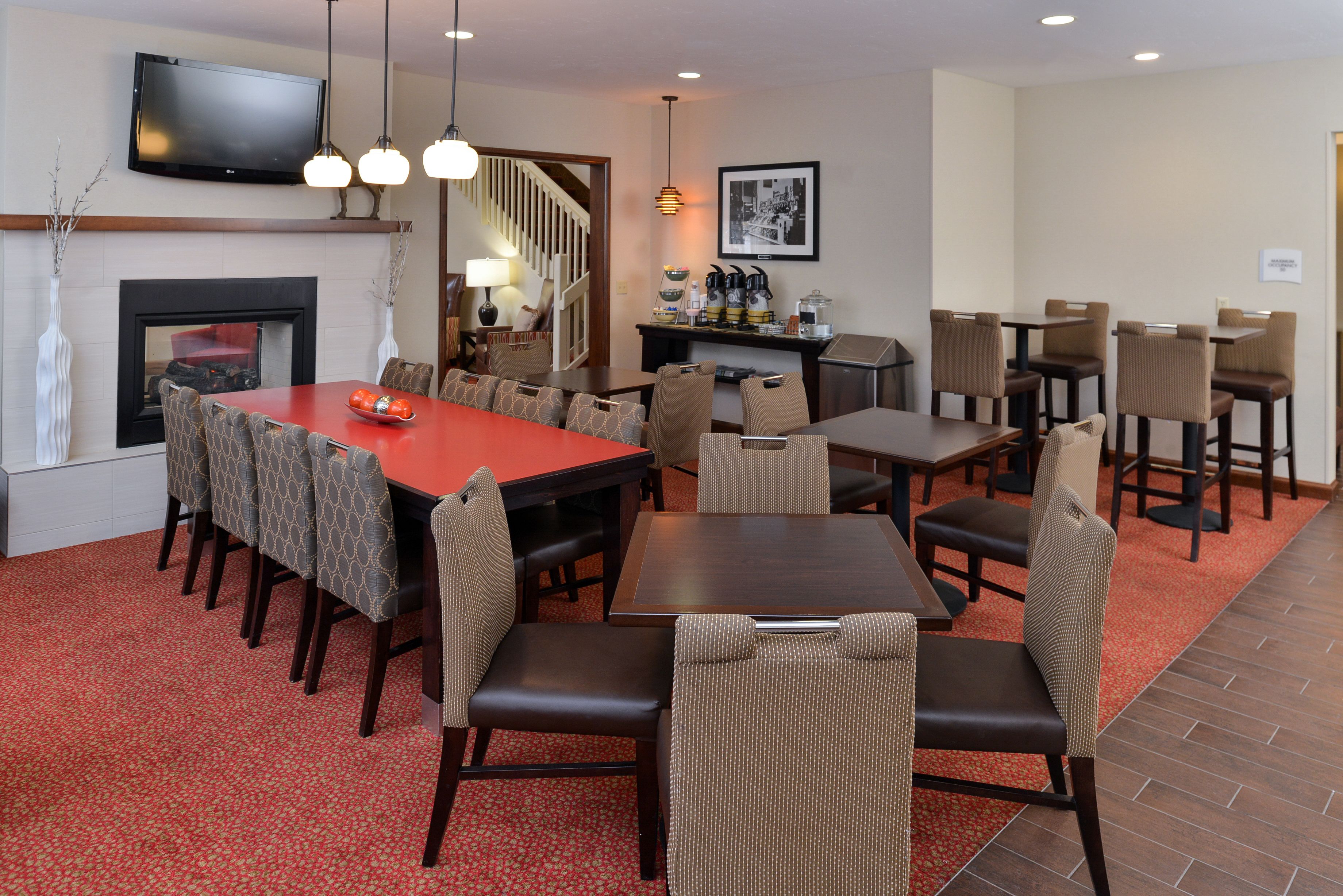 A dining area with a large table, multiple chairs, a fireplace, a television, and a staircase.