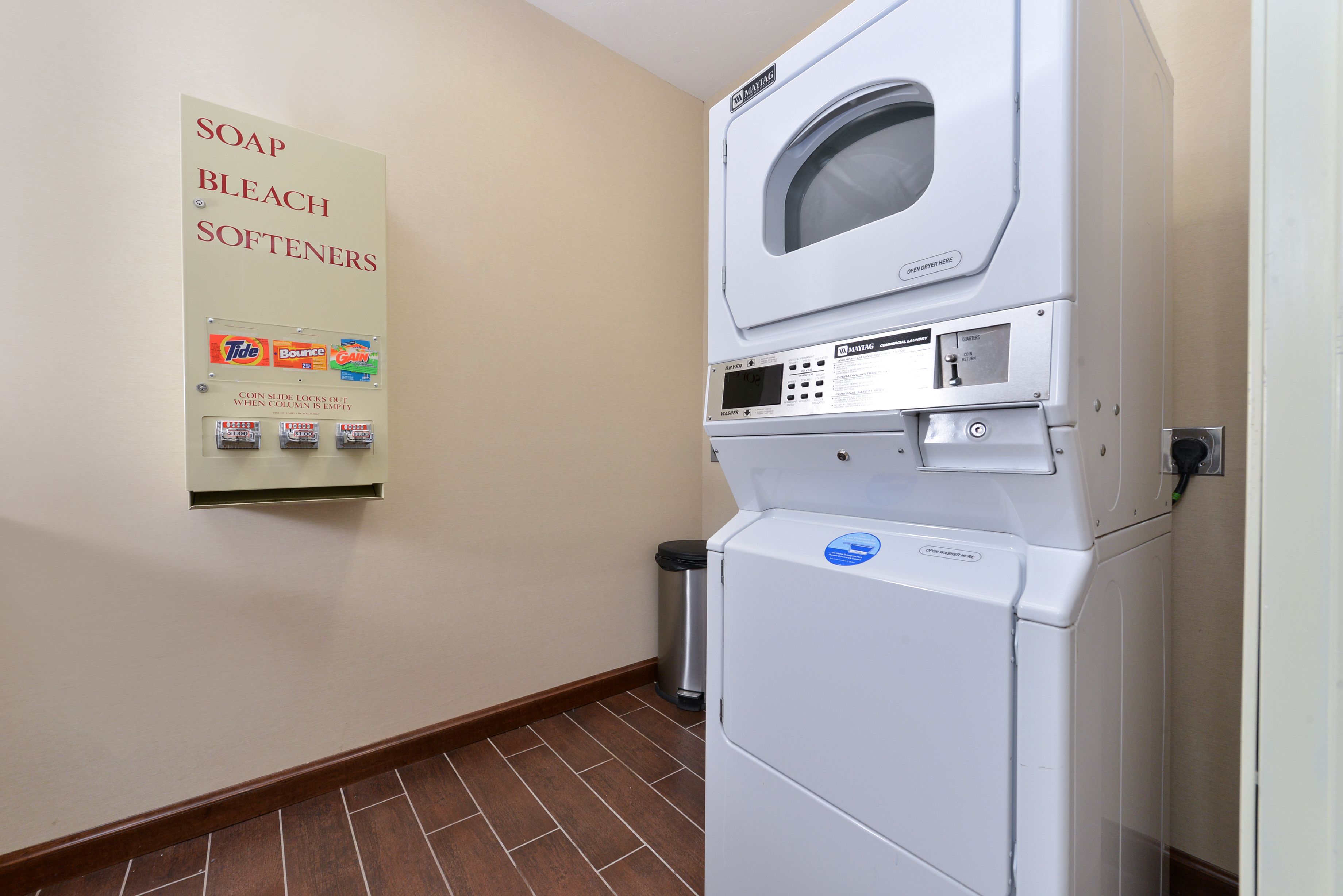 A laundry area with a wall-mounted soap and bleach dispenser and a stacked washer and dryer.