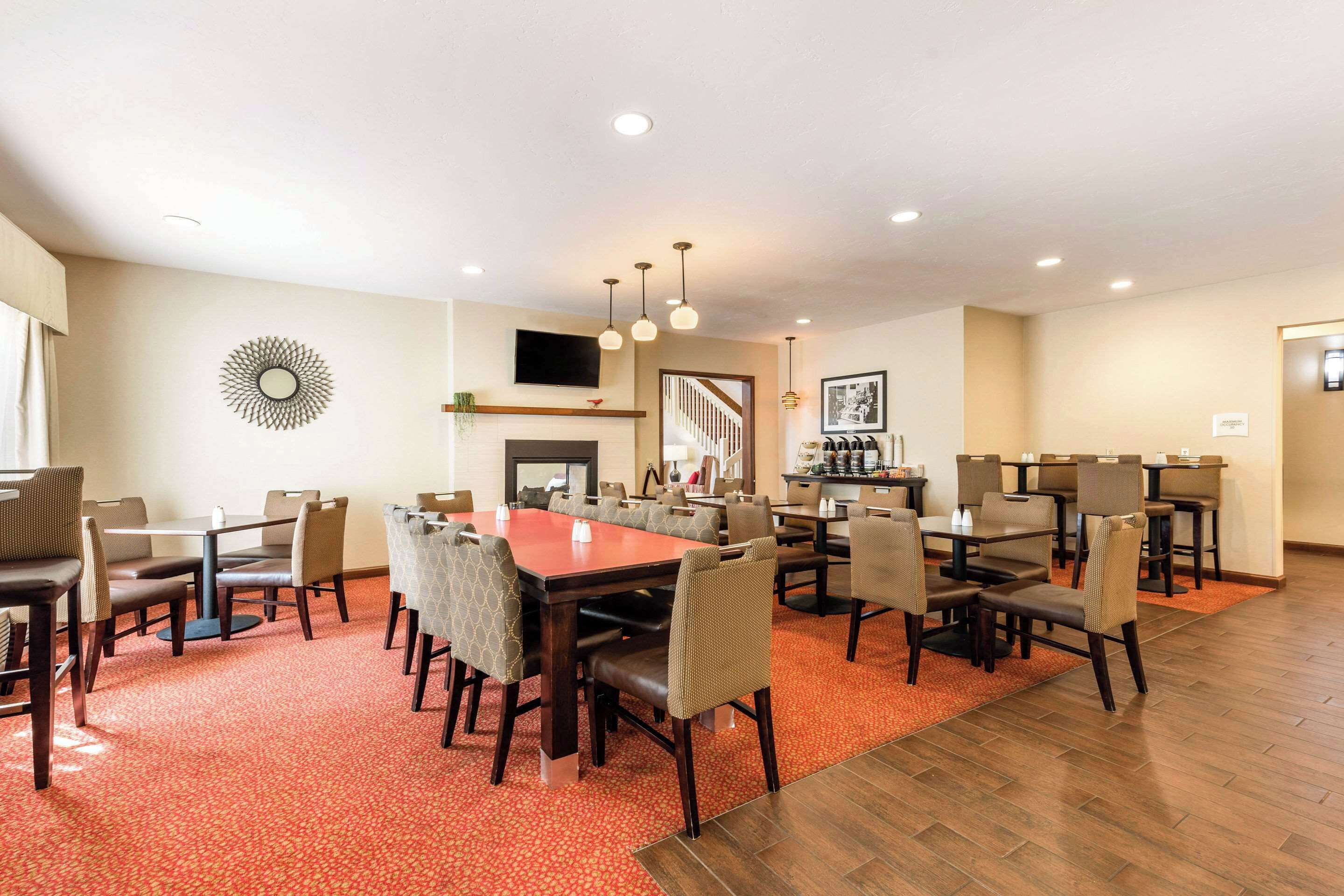 A hotel dining area with multiple tables and chairs, a fireplace, and a staircase leading to another floor.