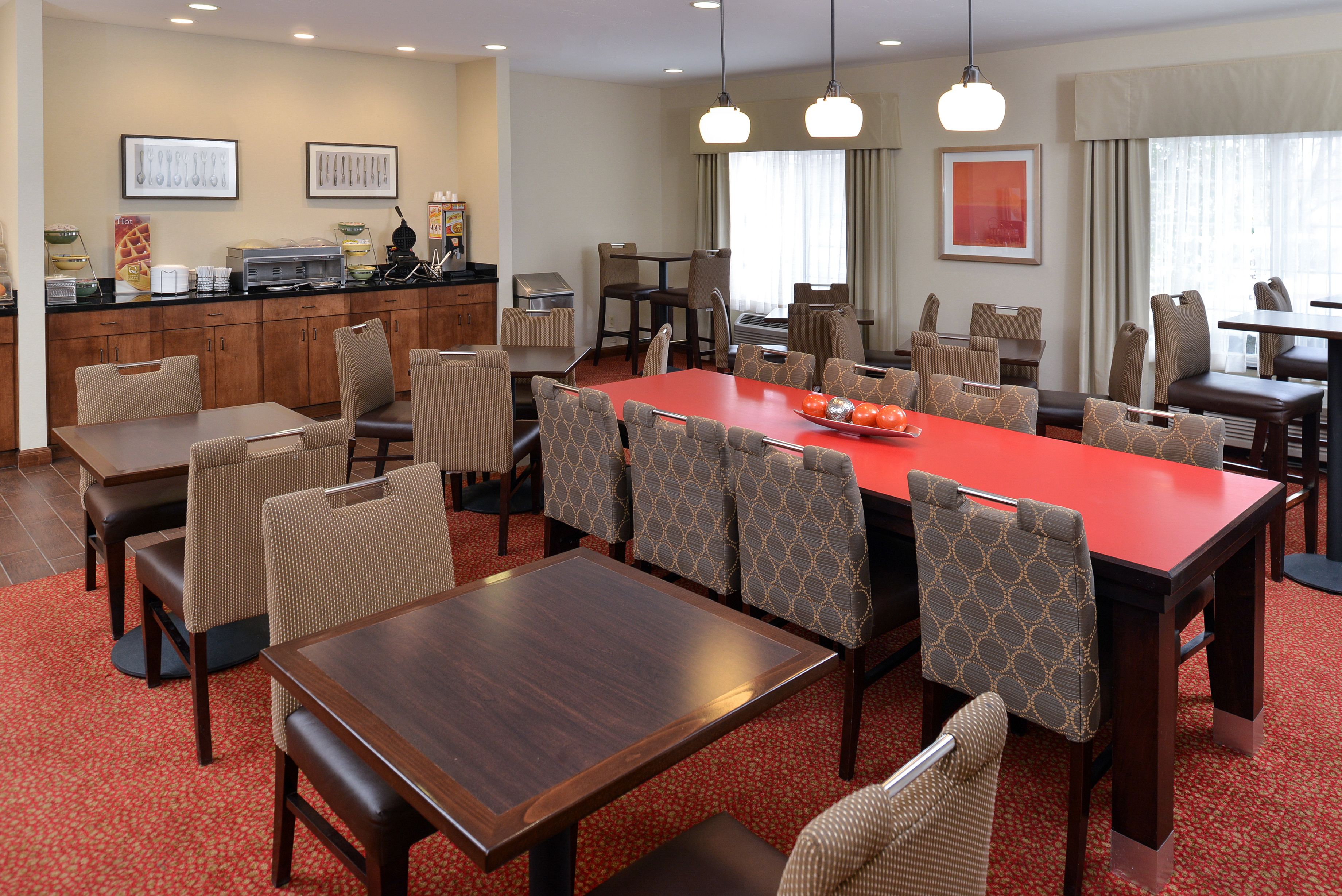 A hotel dining area with a long red table, multiple chairs, and a buffet station.