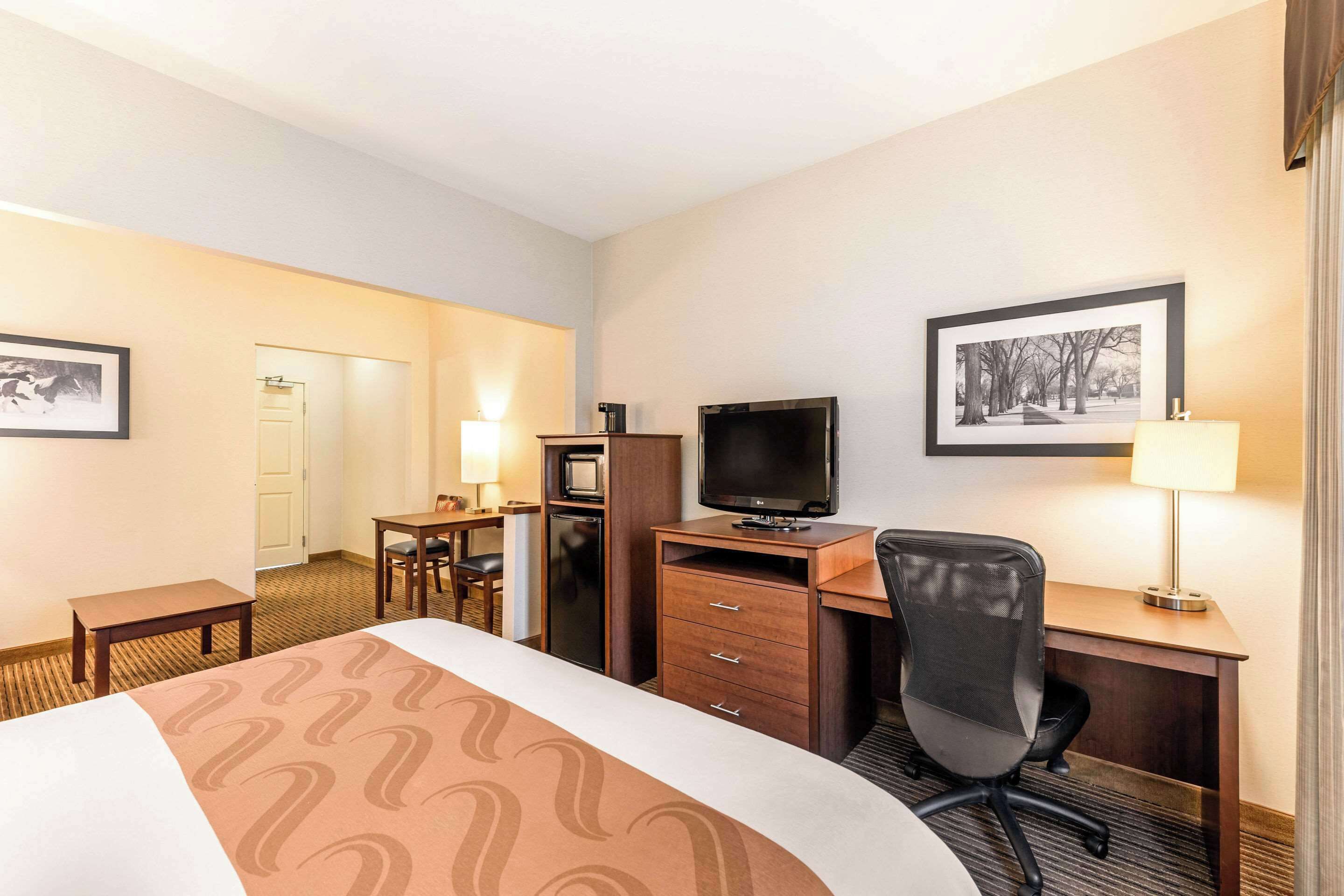 A hotel room with a bed, desk, chair, television, and a small kitchenette.