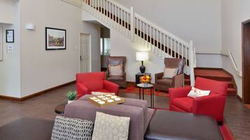 A living room with a staircase, red and brown leather sofas, a small table with a lamp, and a framed picture on the wall.